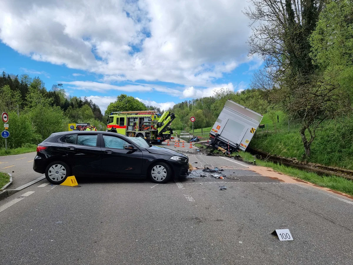 Ein Auto steht nach einem Unfall quer auf der Fahrbahn, und ein Lkw liegt im Bachbett daneben.